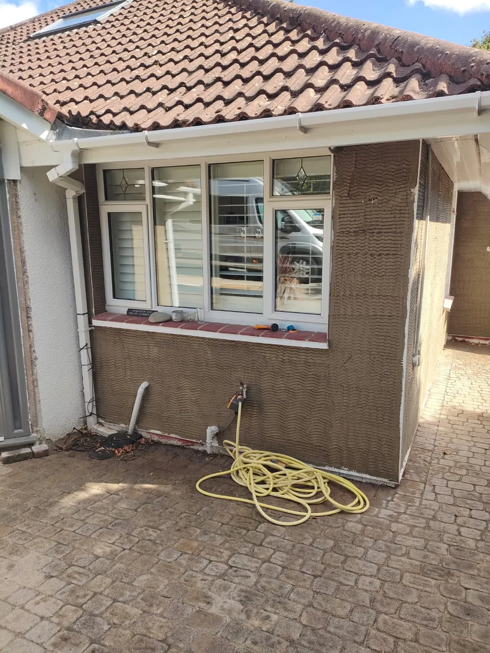 Scratch coat of render around a white window on the front of a bungalow