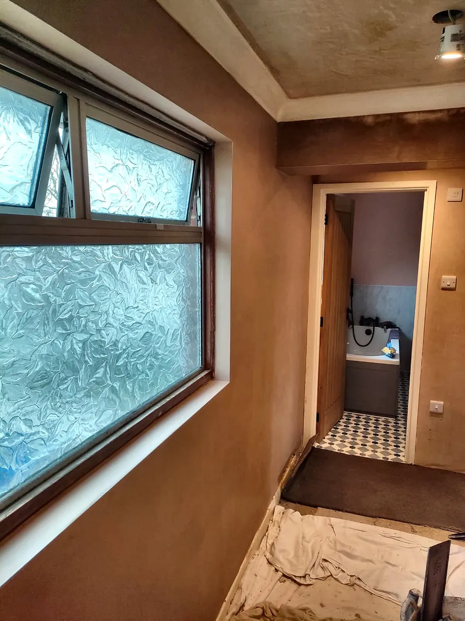 Newly plastered hallway walls and ceiling with a window and bathroom beyond
