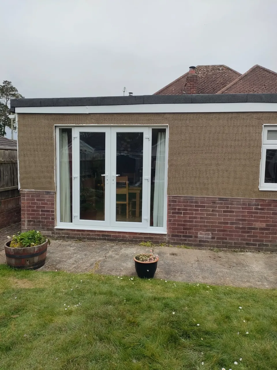 Scratch coat of render on the rear of a bungalow around white French doors above a brick plinth