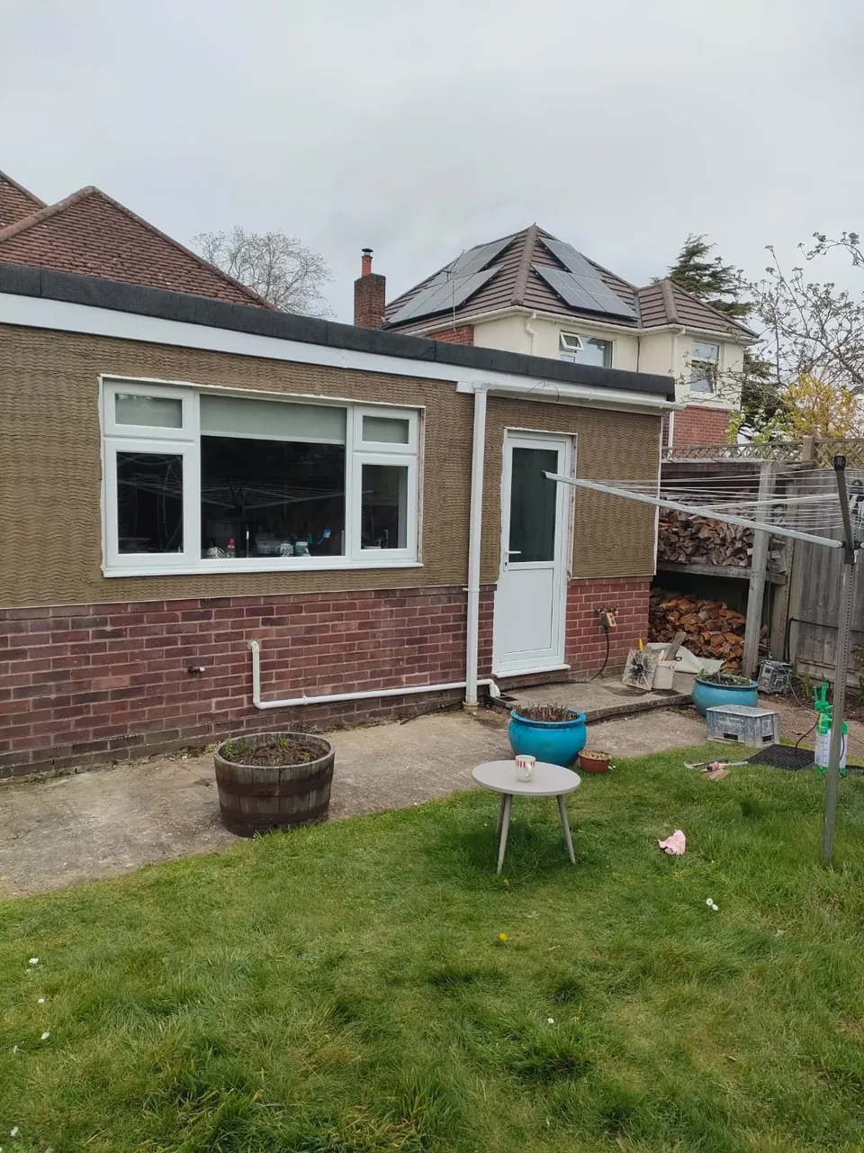 Scratch coat of render on a bungalow with a large window and white door above a brick plinth