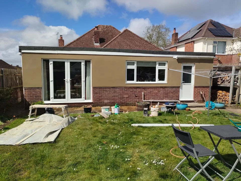 Finished smooth tan render on the rear of a bungalow with French doors, a window and a door above a brick plinth