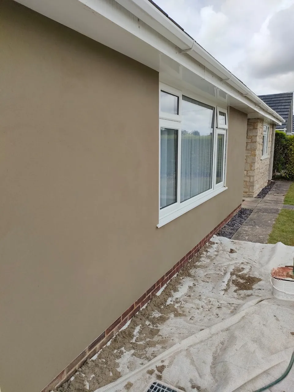 Smooth finished render on the front wall of a bungalow with a large white window and stone clad porch
