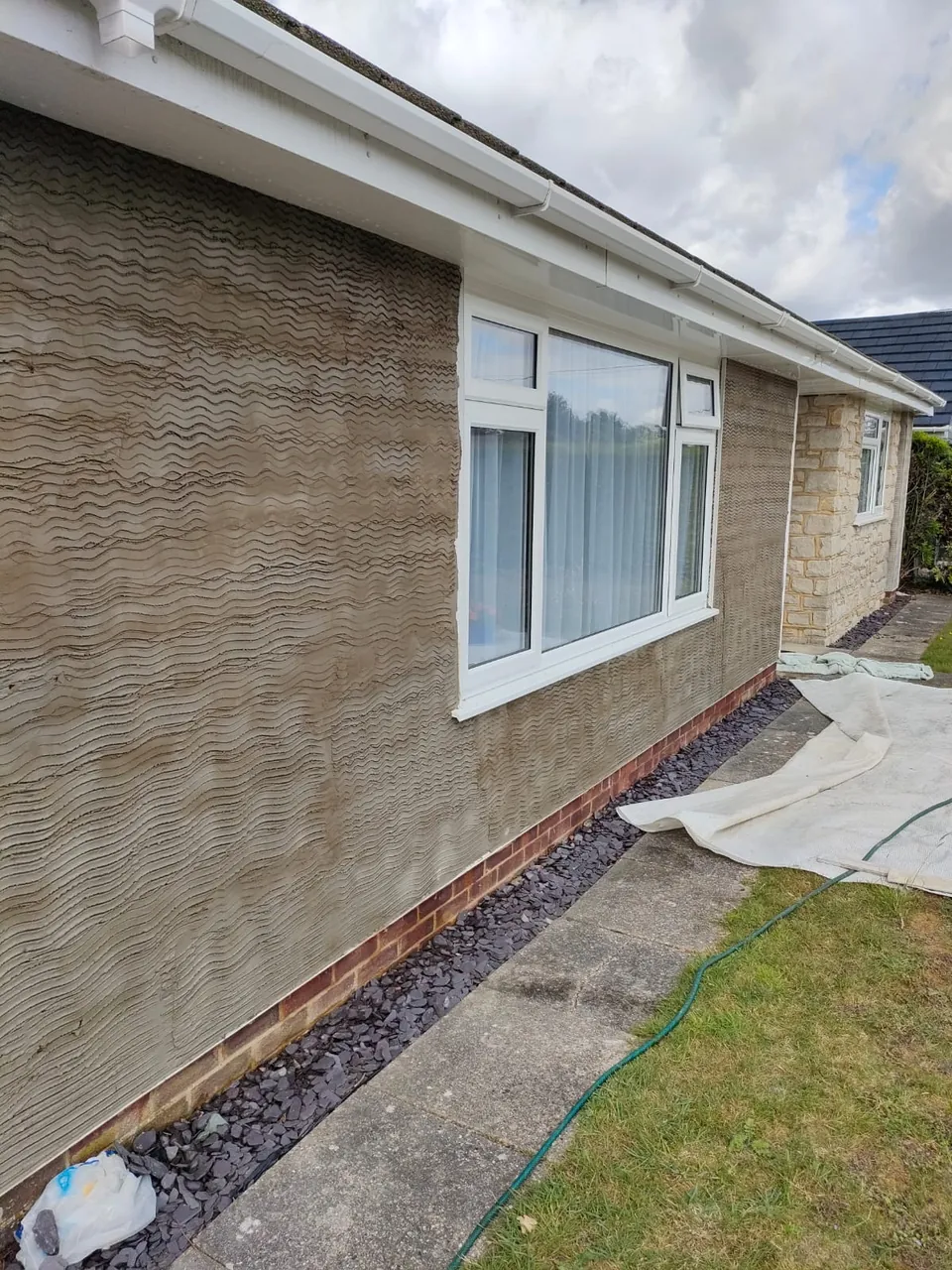 Scratch coat of render across the front wall of a bungalow around a large white window
