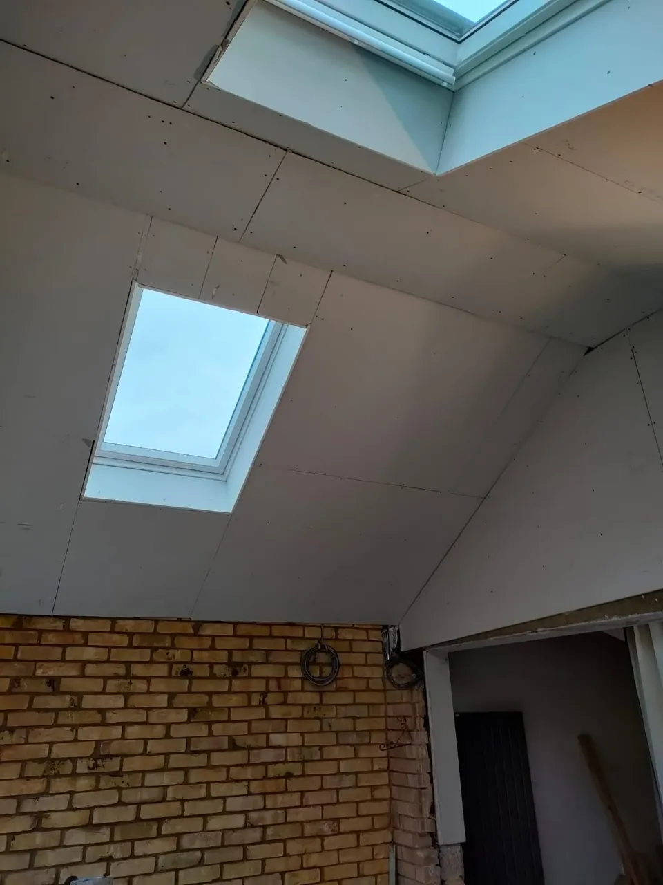 Plasterboarded vaulted ceiling with a roof window above an exposed yellow brick wall